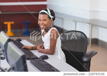 African American child sitting at white desk in bright computer lab, using monitors copy space African American child sitting at white desk in bright computer lab, using monitors copy space 128743140