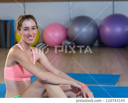 Woman sitting cross?legged on blue yoga mat in gym, with exercise balls and kettlebell, copy space Woman sitting cross?legged on blue yoga mat in gym, with exercise balls and kettlebell, copy space 128743145