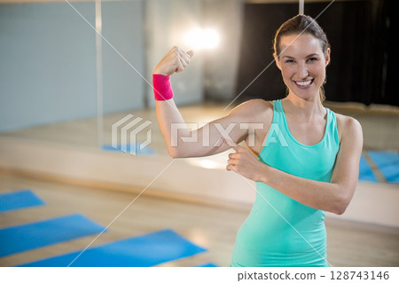 Woman flexing bicep in yoga studio with blue mats and pink wristband, copy space 128743146