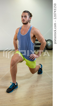 Man performing forward lunge in fitness studio, with stability ball and exercise mats Man performing forward lunge in fitness studio, with stability ball and exercise mats 128743150