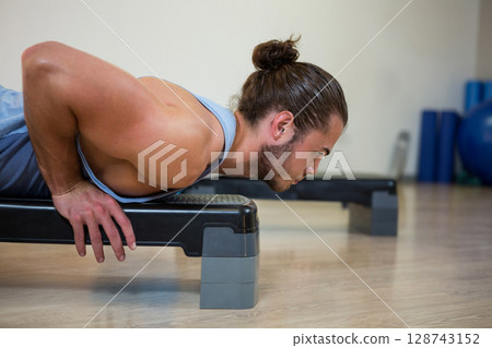 Man performing push?up on step platform in gym with foam rollers, exercise ball, copy space Man performing push?up on step platform in gym with foam rollers, exercise ball, copy space 128743152