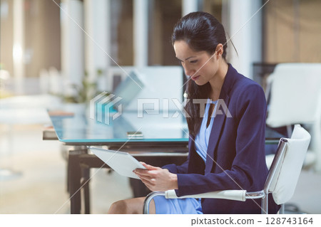 Young Chinese businesswoman reading tablet at glass desk with plant in open plan office, copy space 128743164