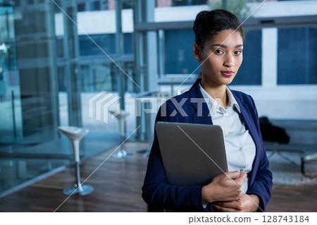 Professional woman holding closed laptop in modern office lounge, with glass walls, copy space Professional woman holding closed laptop in modern office lounge, with glass walls, copy space 128743184