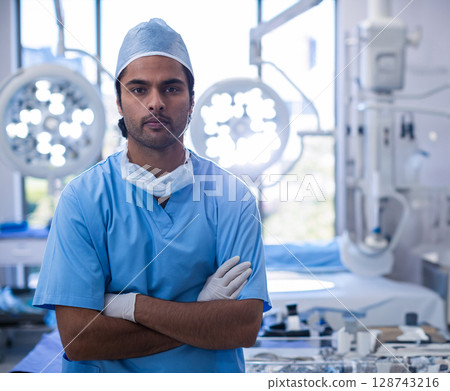 Asian male surgeon crossing arms in operating room, with surgical lights and monitors 128743216