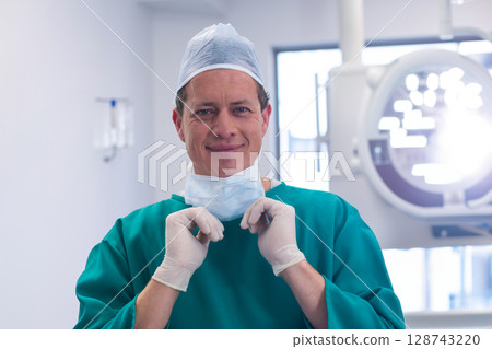Surgeon adjusting surgical mask in operating room, with overhead light and gloves 128743220