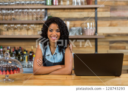 Woman leaning on wooden café counter, showcasing open laptop and glass cake dome with strawberries Woman leaning on wooden café counter, showcasing open laptop and glass cake dome with strawberries 128743293