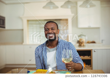 African American man sitting at kitchen table, raising wine glass with plate of corn and veggies African American man sitting at kitchen table, raising wine glass with plate of corn and veggies 128743306