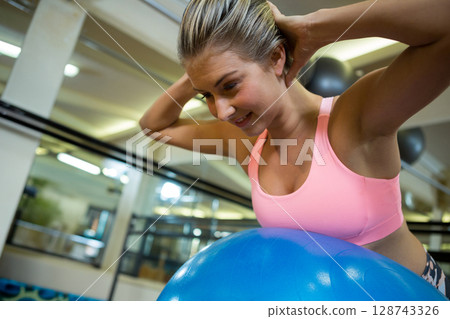 woman doing ab workout on blue stability ball in gym with mirrored wall, copy space 128743326