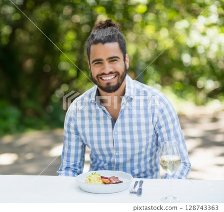Man wearing blue checked shirt sitting outdoors at table, eating meat salad, sipping white wine Man wearing blue checked shirt sitting outdoors at table, eating meat salad, sipping white wine 128743363