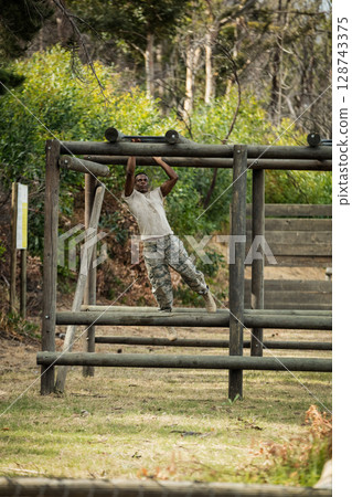 African American man hanging from wooden beams in wooded training area, with wooden ramp African American man hanging from wooden beams in wooded training area, with wooden ramp 128743375