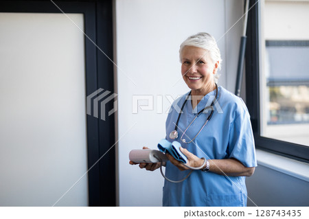 Senior female nurse holding blood pressure monitor and cuff at clinic window, copy space Senior female nurse holding blood pressure monitor and cuff at clinic window, copy space 128743435