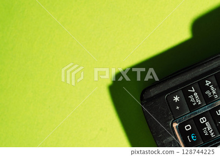 Close-up of retro mobile phone keypad on neon green background with sharp shadows. 128744225
