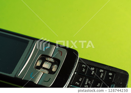 Cropped view of keypad and navigation buttons of an outdated phone on green paper. 128744230