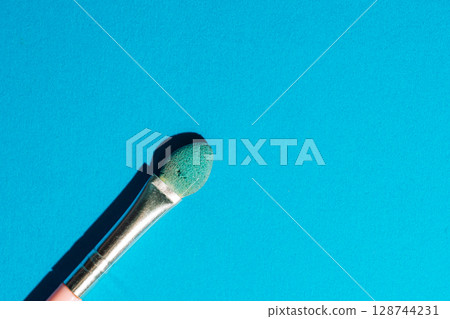 Used green eyeshadow applicator on bold cyan background. Grunge beauty aesthetic meets vibrant pop style. 128744231