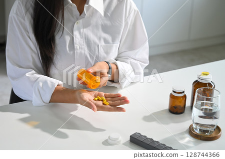 Woman pouring yellow capsules from a pill bottle into her hand. Health care concept Woman pouring yellow capsules from a pill bottle into her hand. Health care concept 128744366