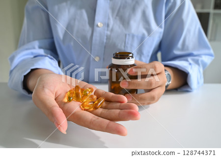 Close up of a person holding fish oil capsules in one hand. Health and nutrition concept Close up of a person holding fish oil capsules in one hand. Health and nutrition concept 128744371
