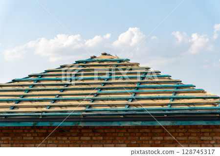 Construction workers prepare a roof with wooden beams and sheathing, showcasing a blend of craftsmanship and open skies 128745317
