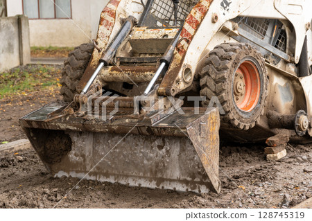A skid steer is prepping the ground at a construction site nestled in nature, signaling ongoing development A skid steer is prepping the ground at a construction site nestled in nature, signaling ongoing development 128745319
