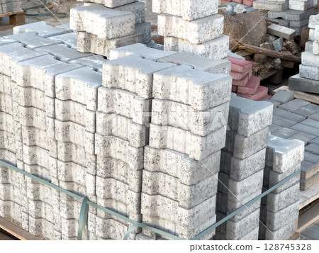 Pallets of gray concrete blocks arranged orderly in a construction area under natural light, showcasing preparation for masonry work 128745328