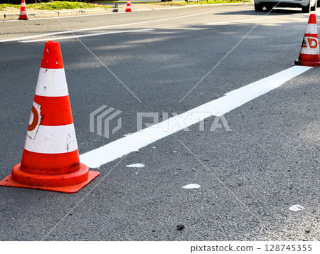 Traffic cones are placed along freshly painted lines on a bustling city street as cars navigate around them during the day 128745355