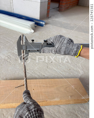 Measuring the diameter of reinforcement using a caliper. Worker's hands in gloves with a caliper at a construction site. 128745381