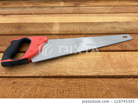 A wood saw lies on a stack of new lumber at a construction site or sawmill. 128745385