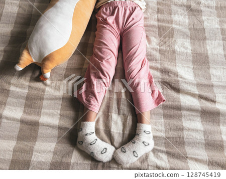 Legs of a girl about 5 years old and plush cat toys on the bed. The child plays on the bed. 128745419
