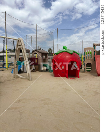 Children's playground with a strawberry-shaped house on a sandy beach. Weekend on the beach with children. Children's playground with a strawberry-shaped house on a sandy beach. Weekend on the beach with children. 128745425