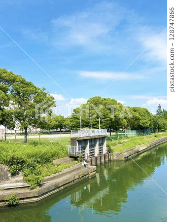 Water gate and river with reflections of trees and blue sky Water gate and river with reflections of trees and blue sky 128747866