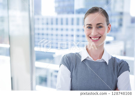 Businesswoman in business attire standing arms crossed on balcony with glass railing, copy space Businesswoman in business attire standing arms crossed on balcony with glass railing, copy space 128748108