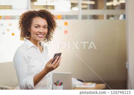 Standing in office, African American woman holding phone near sticky notes on partition, copy space 128748115