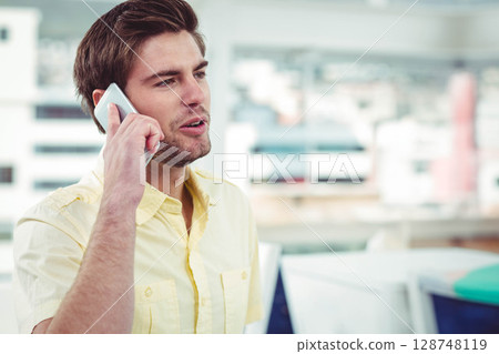 Man in pale yellow shirt speaking on smartphone standing by office desk with binders, copy space Man in pale yellow shirt speaking on smartphone standing by office desk with binders, copy space 128748119