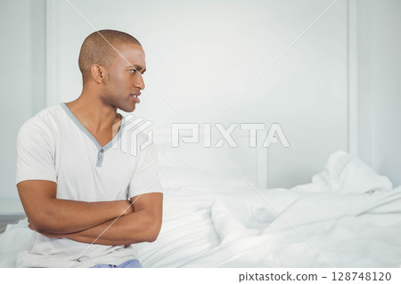 African American man sitting on edge of unmade bed in bedroom with white pillows, copy space African American man sitting on edge of unmade bed in bedroom with white pillows, copy space 128748120