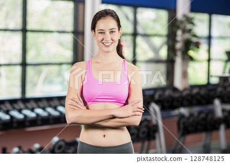 Woman standing at gym by dumbbell rack and potted plant wearing pink sports bra and leggings Woman standing at gym by dumbbell rack and potted plant wearing pink sports bra and leggings 128748125