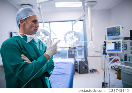 Male surgeon standing beside operating table in operating room checking patient monitor, copy space Male surgeon standing beside operating table in operating room checking patient monitor, copy space 128748143