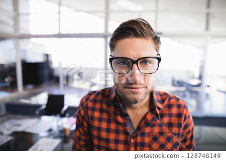 Man standing in modern office wearing glasses and plaid shirt with desks and monitors Man standing in modern office wearing glasses and plaid shirt with desks and monitors 128748149