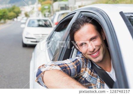 Man in mid-thirties leaning out of white sedan window on suburban street with seatbelt, copy space 128748157