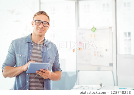 Man in early thirties standing holding tablet in office meeting room with flip chart, copy space 128748238