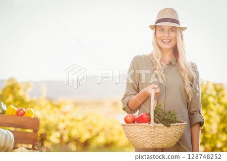 Woman holding basket with tomatoes and herbs in sunlit farm field wearing straw hat, copy space Woman holding basket with tomatoes and herbs in sunlit farm field wearing straw hat, copy space 128748252