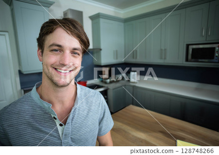 Man smiling and standing beside countertop island in home kitchen near toaster kettle and microwave 128748266