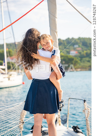 Mother and daughter spending time together on the bow of a sailing yacht. Family bonding, sea adventure, and peaceful travel lifestyle Mother and daughter spending time together on the bow of a sailing yacht. Family bonding, sea adventure, and peaceful travel lifestyle 128748267