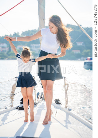 Mother and daughter spending time together on the bow of a sailing yacht. Family bonding, sea adventure, and peaceful travel lifestyle Mother and daughter spending time together on the bow of a sailing yacht. Family bonding, sea adventure, and peaceful travel lifestyle 128748279