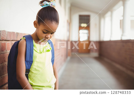 African American boy standing in school hall wearing hair bow, carrying blue backpack, copy space African American boy standing in school hall wearing hair bow, carrying blue backpack, copy space 128748333