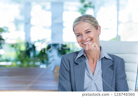 Senior woman sitting on high-back chair at conference table smiling with potted plants, copy space Senior woman sitting on high-back chair at conference table smiling with potted plants, copy space 128748360