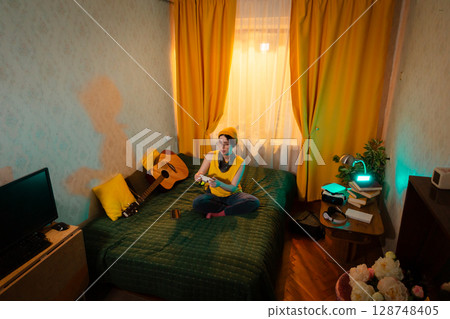 Caucasian teen girl spending free time playing games on her bed, surrounded by pillows. Concept of youth identity and gaming habits. Top view, wide shot Caucasian teen girl spending free time playing games on her bed, surrounded by pillows. Concept of youth identity and gaming habits. Top view, wide shot 128748405
