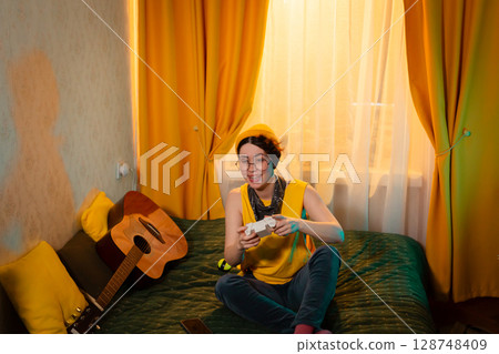 Girl in casual clothes laughs while holding a controller in bright room. Concept of gaming enjoyment and cozy lifestyle. Wide shot Girl in casual clothes laughs while holding a controller in bright room. Concept of gaming enjoyment and cozy lifestyle. Wide shot 128748409