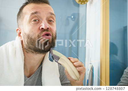 Man shaving trimming his beard Man shaving trimming his beard 128748807