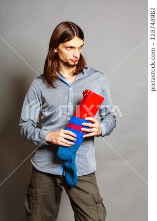 Guy putting wrapped gift in knitted christmas sock Guy putting wrapped gift in knitted christmas sock 128748982