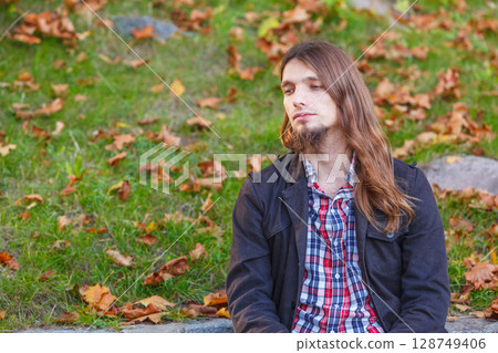 Man long hair sitting on bench in autumn park Man long hair sitting on bench in autumn park 128749406