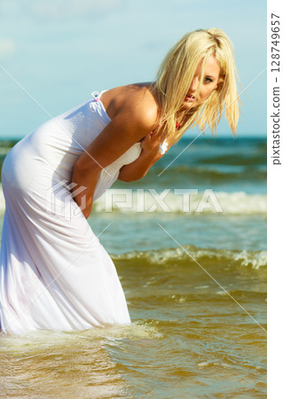 Blonde woman wearing dress walking in water 128749657